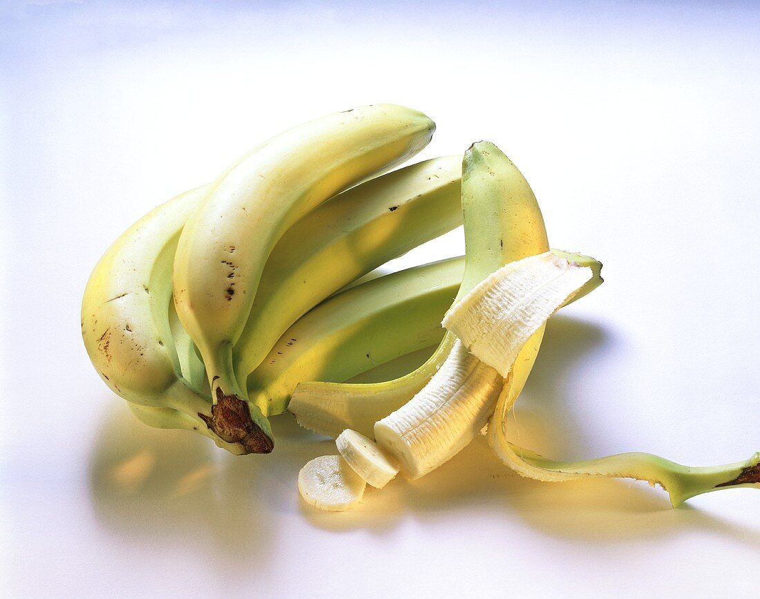 A bunch of bananas and a peeled banana, cut into