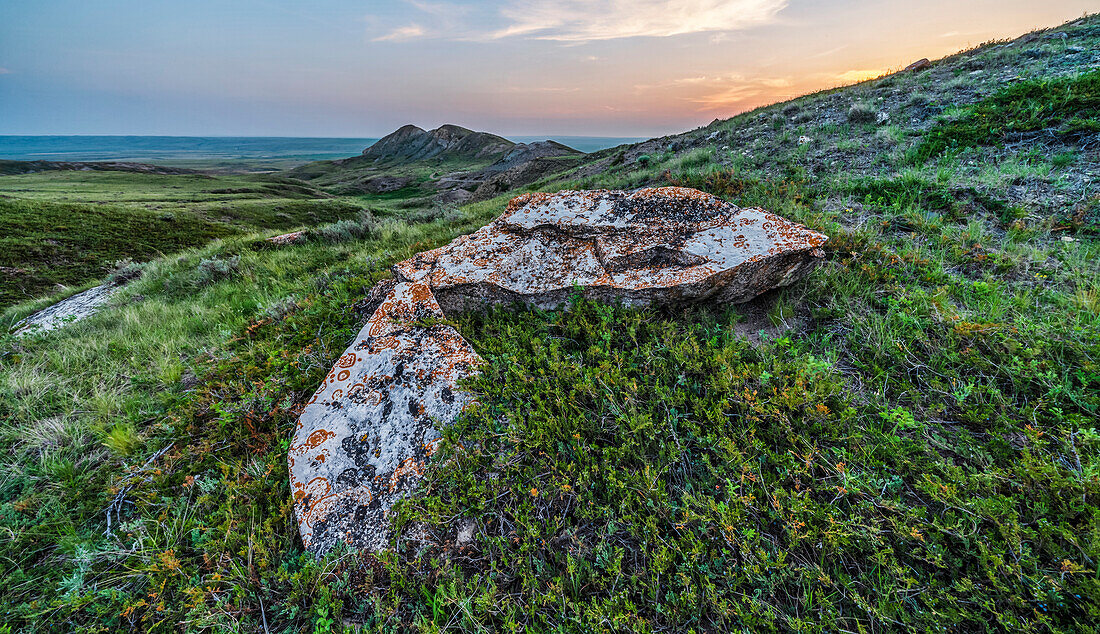 Sonnenuntergang über dem Horizont mit einem Felsen im Vordergrund, Grasslands National Park; Val Marie, Saskatchewan, Kanada
