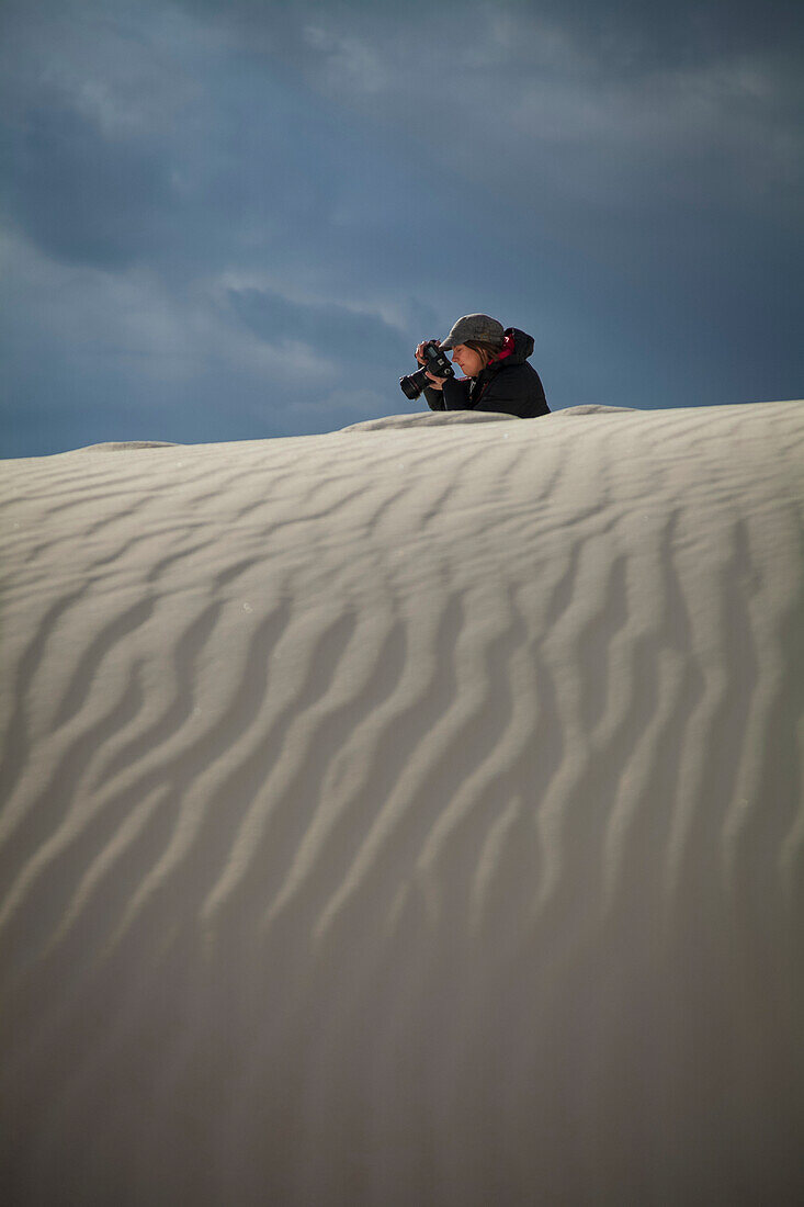 Weibliche Fotografin macht ein Foto mit weißem Sand im Vordergrund, White Sands National Monument; Alamogordo, New Mexico, Vereinigte Staaten von Amerika.