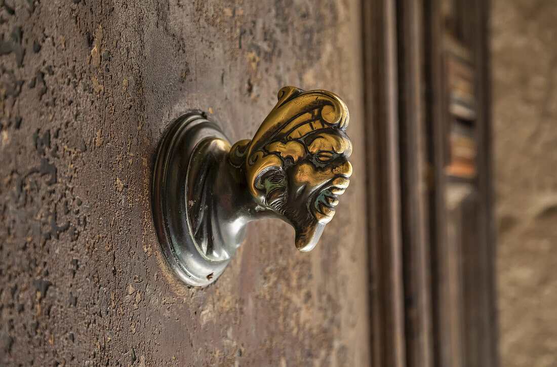 Brass decorative knob of a human head and face mounted on a concrete wall; Venice, Italy