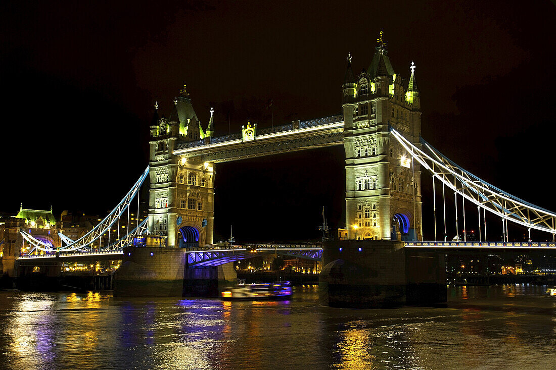 Tower Bridge bei Nacht beleuchtet und reflektiert im ruhigen Wasser der Themse; London, England.