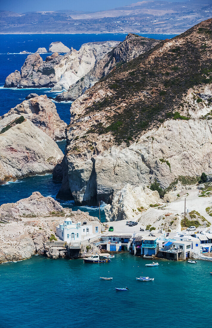 Fyropotamos Village with boats in the small harbour and a view of the rugged coastline; Fyropatamos, Milos Island, Cyclades, Greece