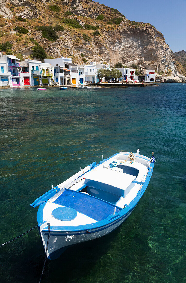 Boat moored in the water in Klima village with white houses and colourful accents along the water's edge; Klima, Milos Island, Cyclades, Greece