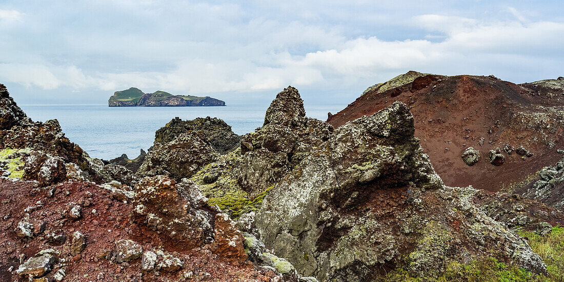 Zerklüftete Felsen entlang der Küste der Insel Heimaey, mit Blick auf die Insel Ellioaey, Teil einer Inselgruppe entlang der Südküste Islands; Vestmannaeyjar, Südregion, Island.