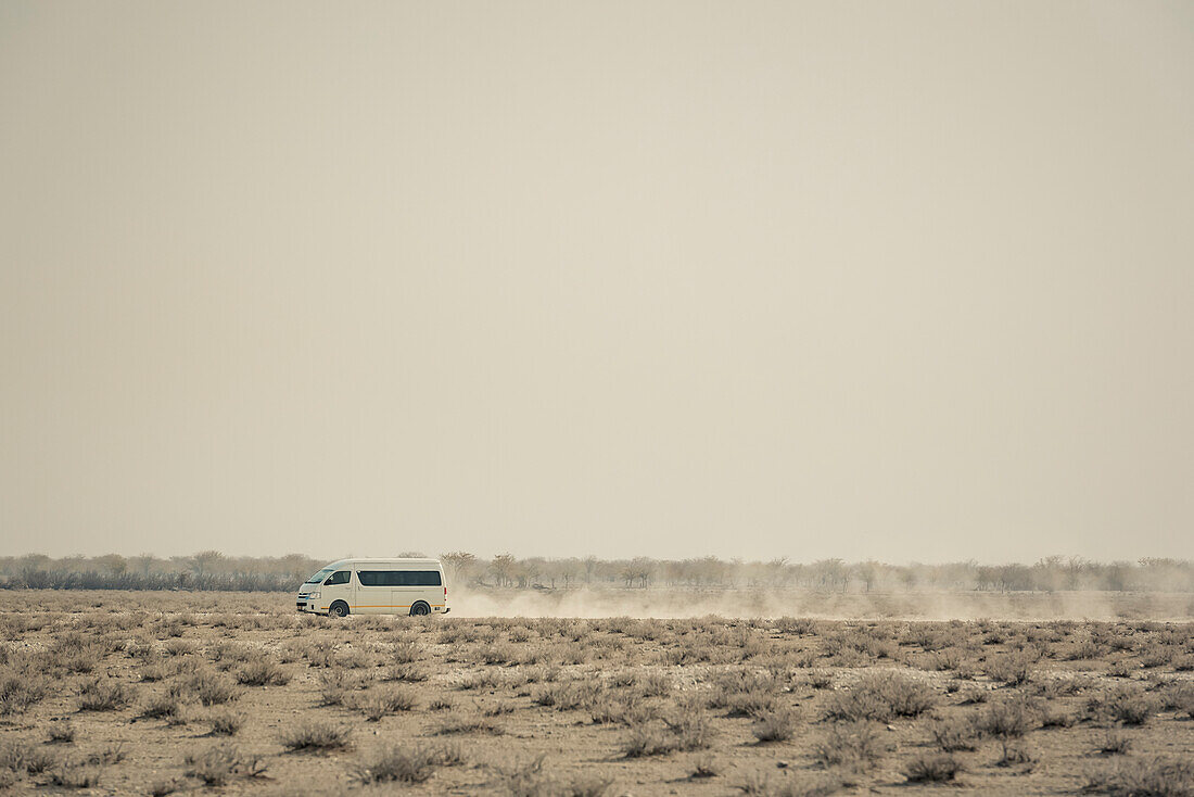 Ein Fahrzeug fährt auf einer staubigen Straße, Etosha-Nationalpark; Namibia.