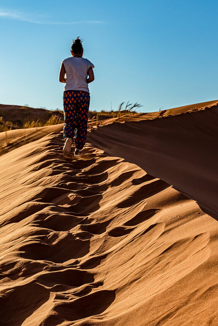 Weibliche Touristin geht eine Sanddüne hinauf, Elim-Düne, Namib-Wüste; Sesriem, Namibia.