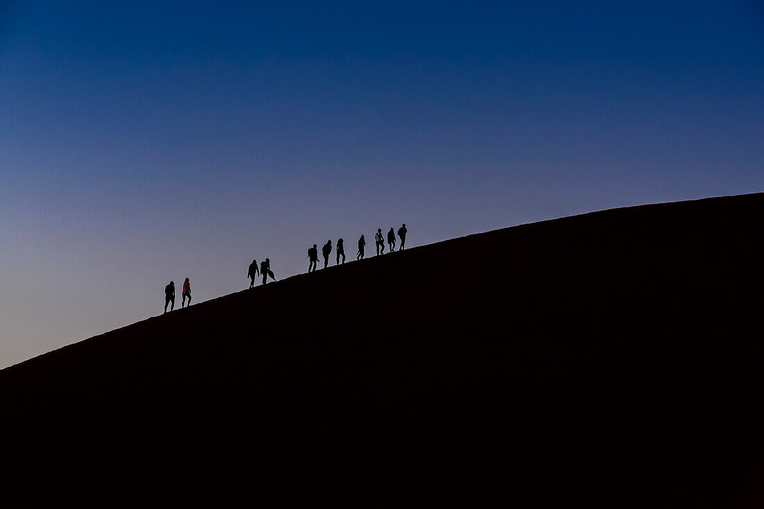 Silhouette of tourists climbing Dune 45 at dusk, Sossusvlei, Namib Desert; Namibia