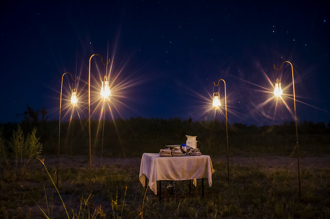 Dinner table for safari guests, surrounded by lights at dusk in Botswana Moremi Game Reserve; Okavango Delta, Botswana