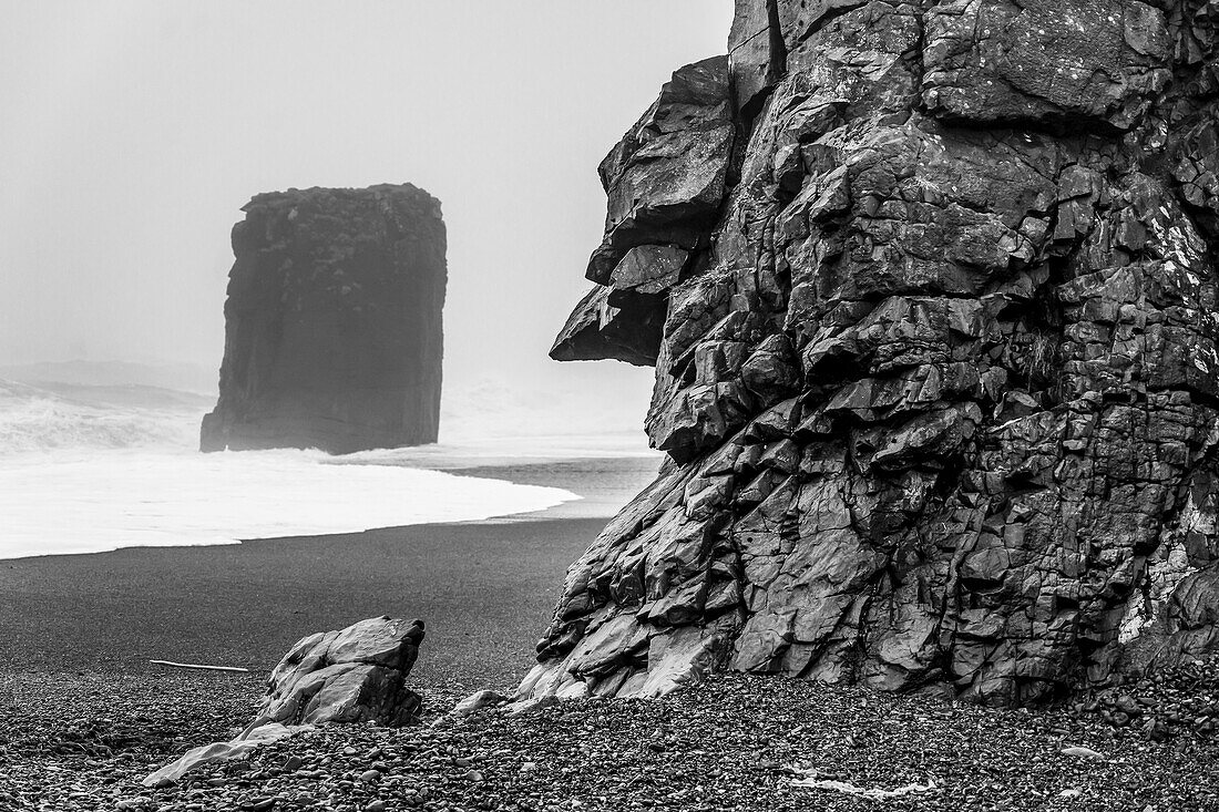Schwarz-Weiß-Bild eines Meeresstapels entlang der zerklüfteten Küste von Ostisland; Djupivogur, Ostregion, Island.