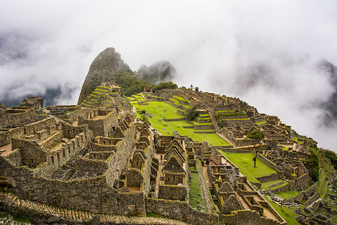 Die heilige Stadt Machu Picchu im Sonnenlicht und in tief hängende Wolken gehüllt; Cusco, Peru