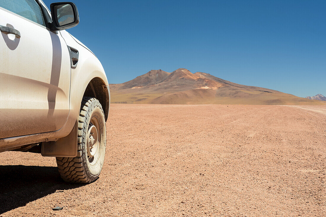Four-wheel drive vehicle seen from the side and showing off-road tire with high altitude desert and mountains in the background; Potosi, Bolivia