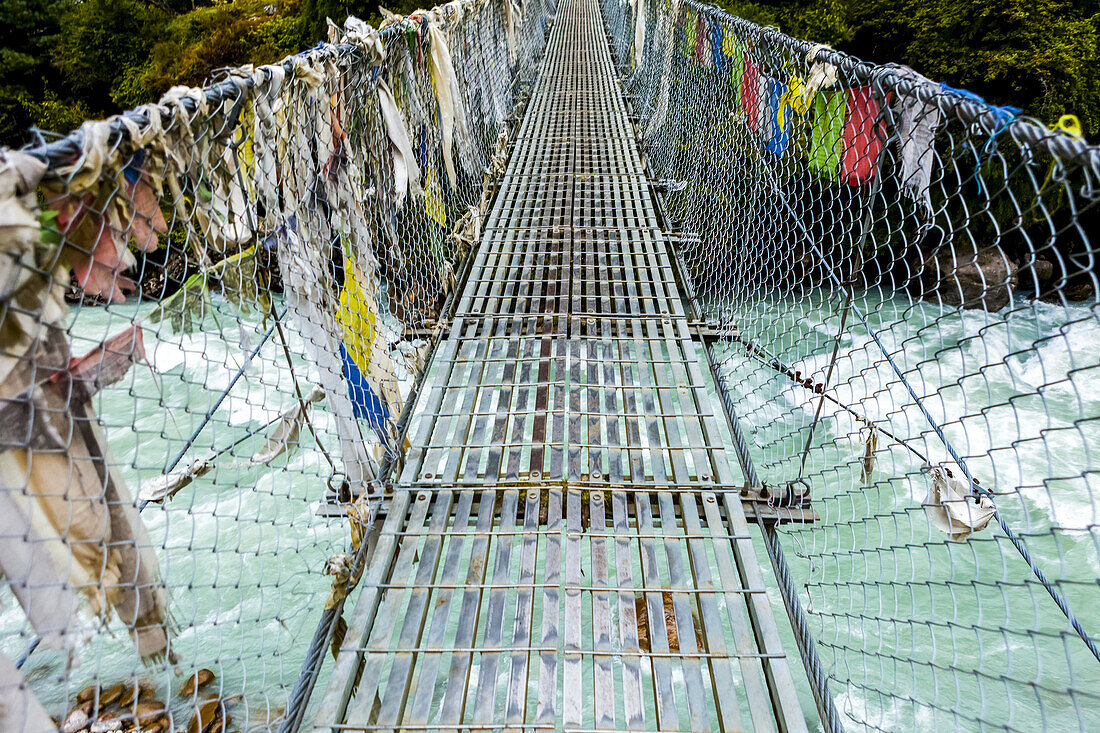 Prayer flags line each side of the suspension bridge over the Dudh Koshi River along the Everest Base Camp and Gokyo trek trail; Solokhumbu District, Nepal