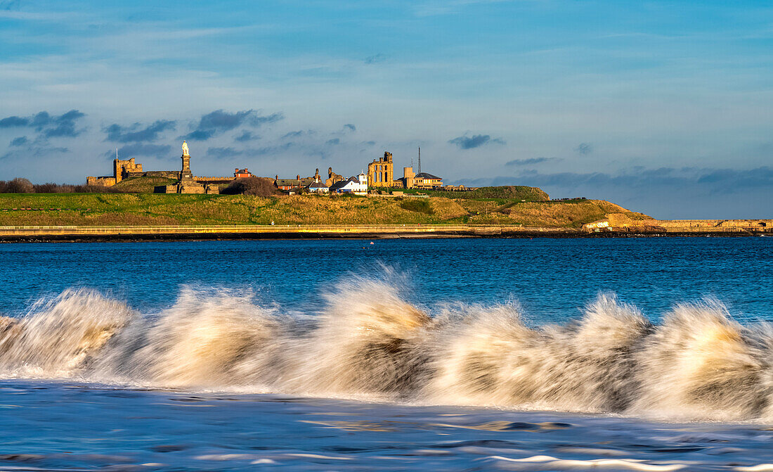 North Sea waves breaking on the shore of South Shields with the historic buildings and town of Tynemouth in the background; South Shields, Tyne and Wear, England, United Kingdom.