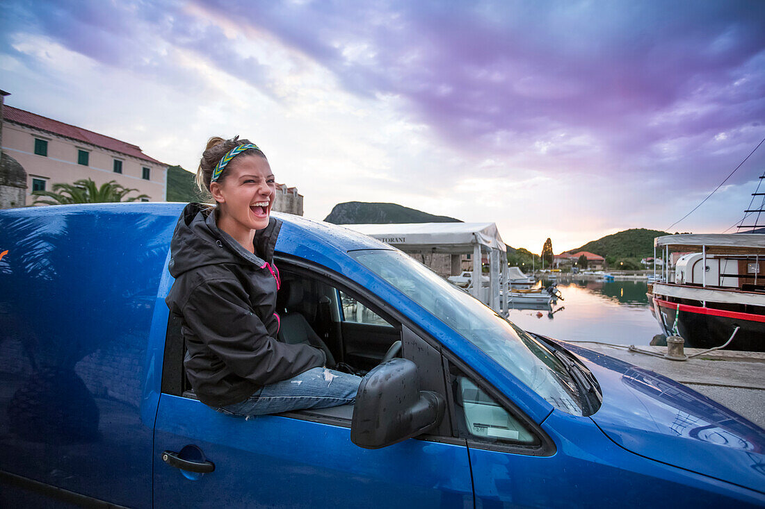 Eine junge Frau sitzt in der Abenddämmerung am Fenster eines Autos am Hafen. Die am See gelegene Stadt Mali Ston in Kroatien ist eine historische Festung mit einer Mauer. Die Stadt ist auch berühmt für frische Austern; Mali Ston, Dubrovacko-neretvanska zupanija, Kroatien