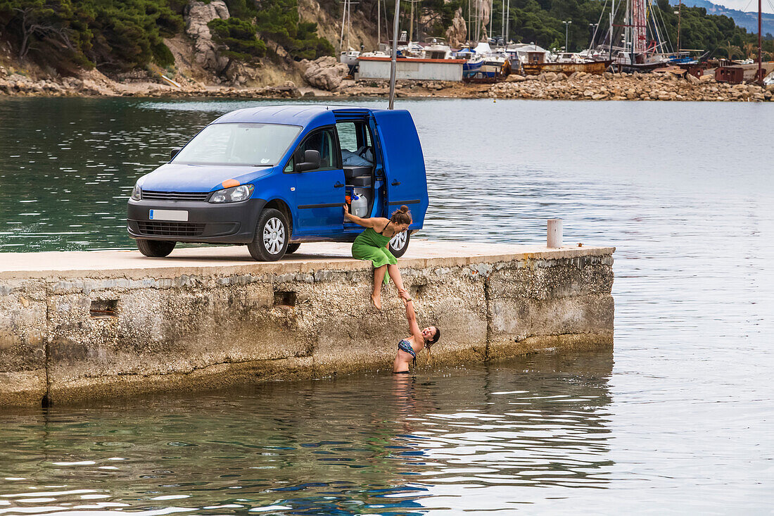 Women stop for an early morning swim and shower after camping in their van; Podgora, Split-Dalmatia County, Croatia