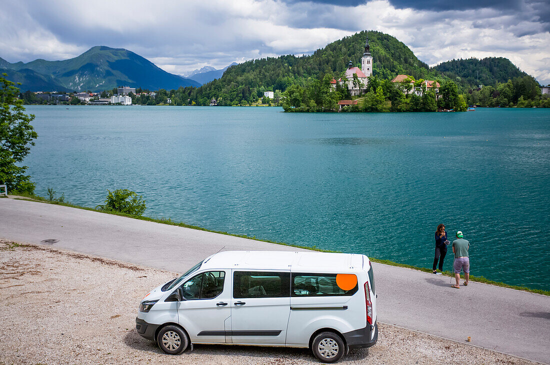 Reisende halten ihr Wohnmobil an, um ein Foto von der Kirche auf einer Insel (The Church of the Assumption) im Bleder See zu machen; Bled, Slowenien