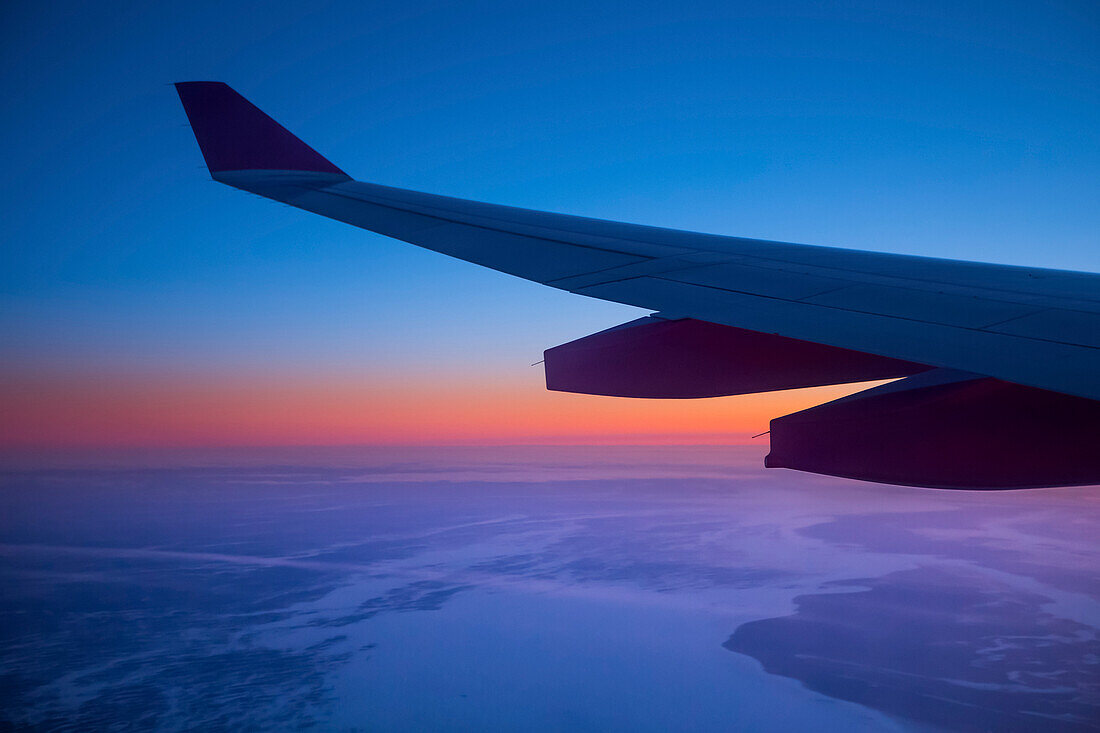 Detail eines Flugzeugflügels beim Überfliegen der arktischen Meere auf dem Weg nach Island mit einem leuchtend rosa Himmel am Horizont; Island