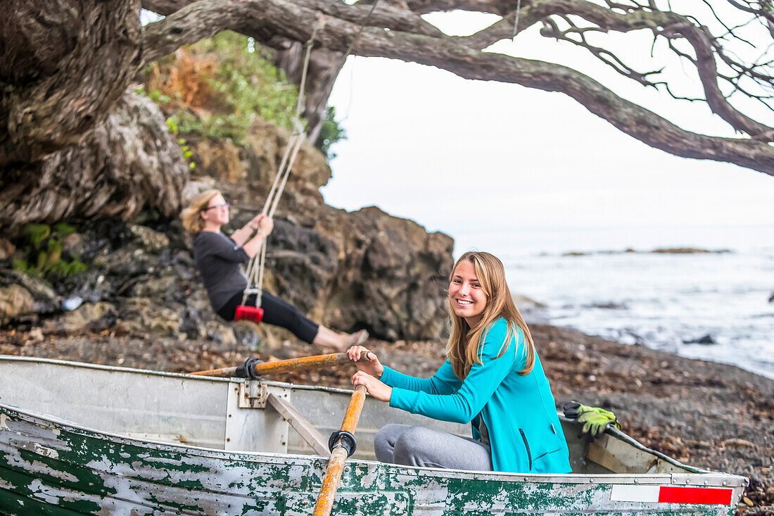 Girls sit and play in a beached boat on the eastern cape of New Zealand; Te Kaha, Bay Of Plenty, New Zealand