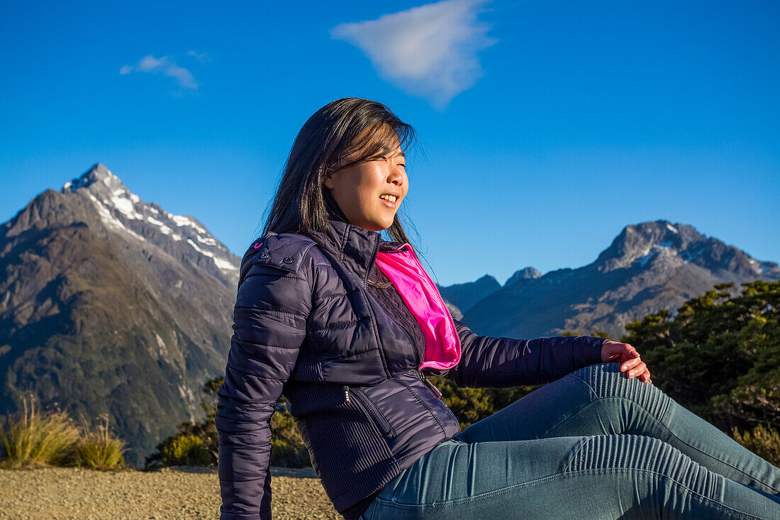 A woman relaxes at the summit during a hike through the Key Summit Track as part of the Routeburn track in the Fiordland National Park; Southland, New Zealand