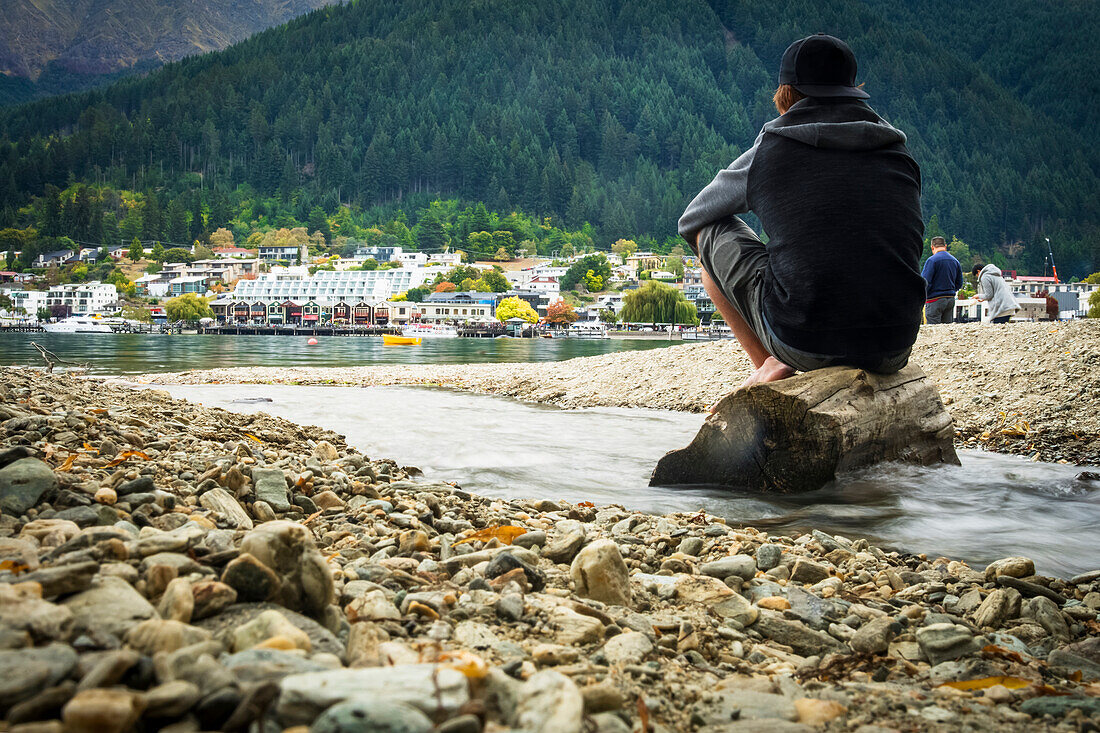A man sits and reflects on the shores of Queenstown's Lake Wakatipu; Queenstown, Otago, New Zealand