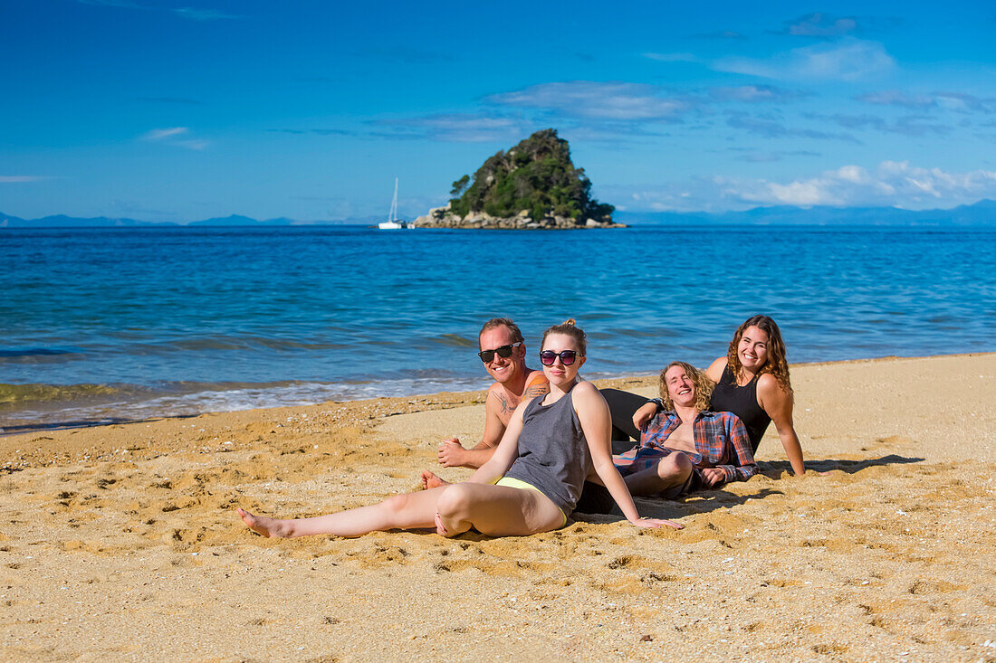 A group of friends sitting on the golden sand beaches of New Zealand's Abel Tasman National Park; Tasman, New Zealand