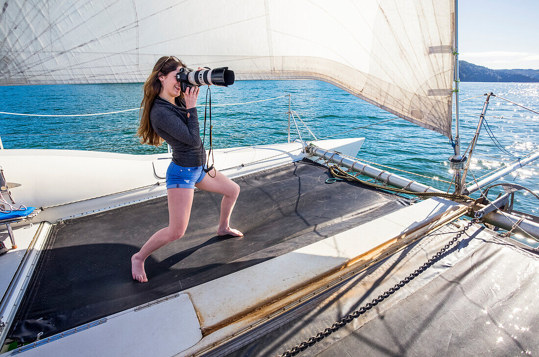 Frau steht auf einem Katamaran und fotografiert mit einer Kamera mit Teleobjektiv auf einer Bootstour durch den Abel Tasman National Park; Tasman, Südinsel, Neuseeland.