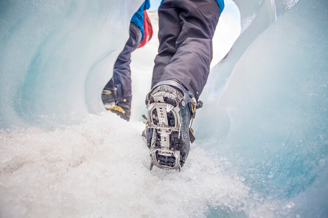 Nahaufnahme der Füße einer Person, die Stollen mit Stacheln trägt, während sie auf dem Eis des berühmten Franz Josef Gletschers läuft; Westküste, Neuseeland