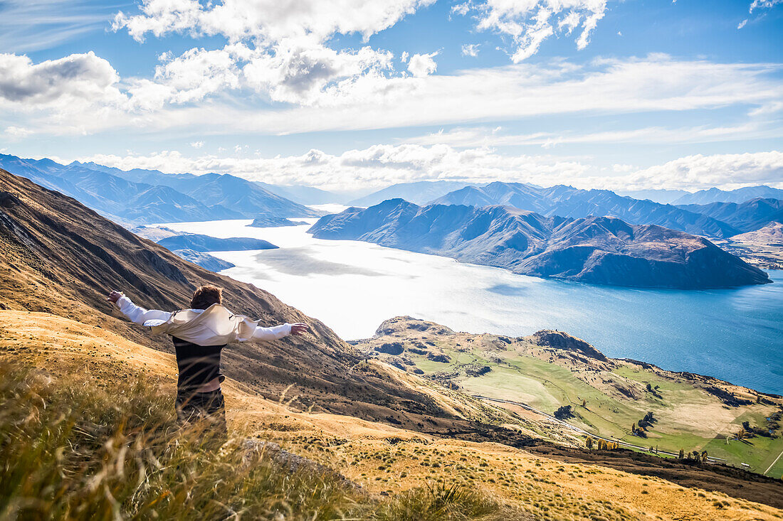 The strenuous yet highly rewarding hike to Roys Peak in Wanaka. The hike is difficult but the views are spectacular. A traveler celebrates at the summit; Wanaka, Otago, New Zealand