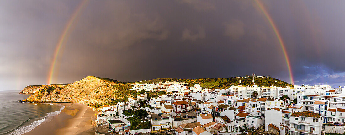 Regenbogen über dem traditionellen Fischerdorf Burgau unter einem stürmischen Himmel in der Gemeinde Vila do Bispo in der westlichen Region der Algarve; Burgau, Algarve, Portugal
