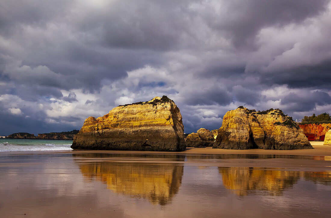 Dona Ana Beach at low tide with its rocky sandstone shoreline and sea stacks along the famous Algarve coastline under a stormy sky; Praia da Dona Ana, Lagos, Algarve Region, Portugal