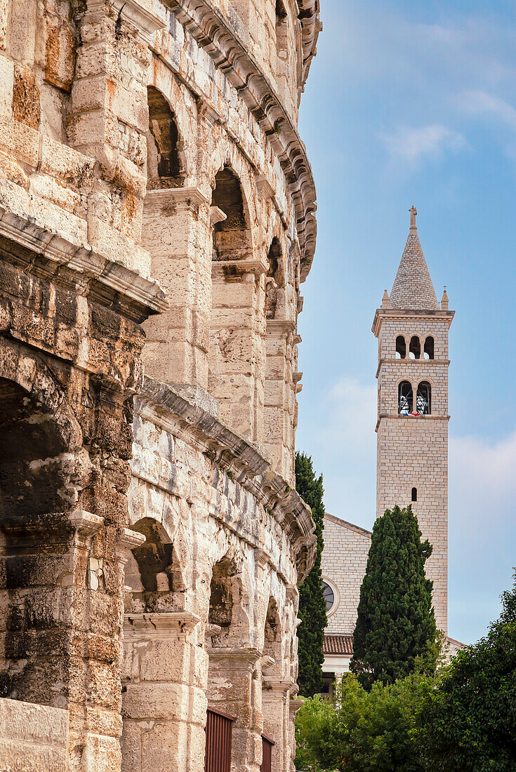 Die Arena von Pula, 1. Jahrhundert, römisches Amphitheater und der Glockenturm der Kirche und des Klosters des Heiligen Antonius von Padua im Hintergrund mit blauem Himmel; Pula, Istrien, Kroatien.