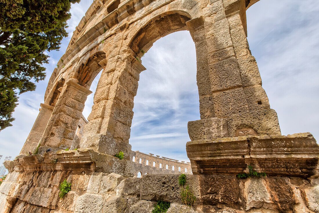 Close-up of the Pula Arena, 1st Century Roman Amphitheatre, looking through the arches with a cloudy, blue sky; Pula, Istria, Croatia