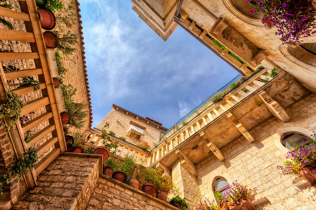 Looking up at the balconies lined with potted plants and the yellow stonework of the 11th Century, Benedictine Monastery of St Nicholas on the medieval island town of Trogir; Trogir, Croatia