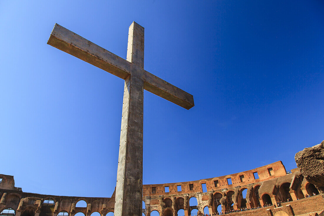 Nahaufnahme eines christlichen Kreuzes im Inneren des römischen Kolosseums vor blauem Himmel, das der Papst im Jahr 2000 zum Gedenken an die christlichen Märtyrer errichten ließ; Rom, Latium, Italien