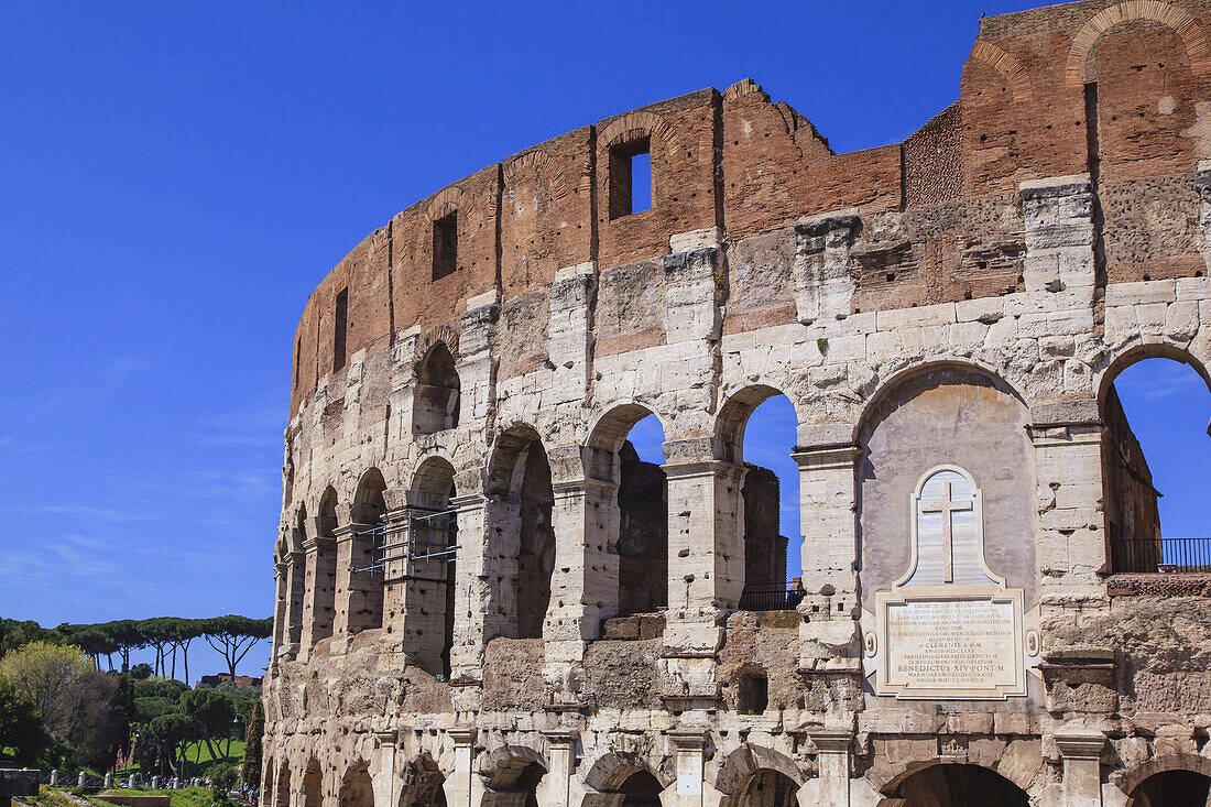 Nahaufnahme des Kolosseums vor blauem Himmel, mit einer Marmortafel über dem Osteingang, die den christlichen Märtyrern gewidmet ist; Rom, Latium, Italien.