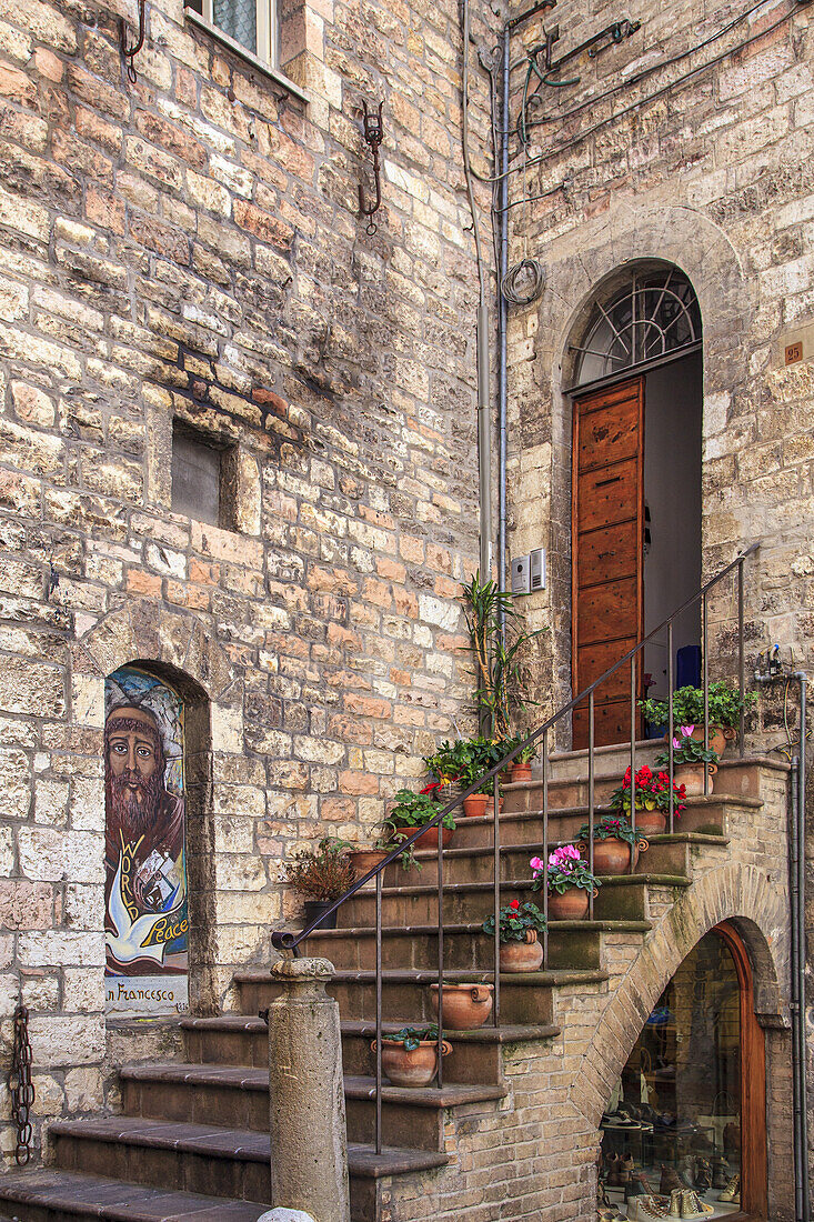 Treppe und Eingang eines alten Steingebäudes mit bunten Blumentöpfen, die die Stufen säumen; Volterra, Provinz Pisa, Toskana, Italien