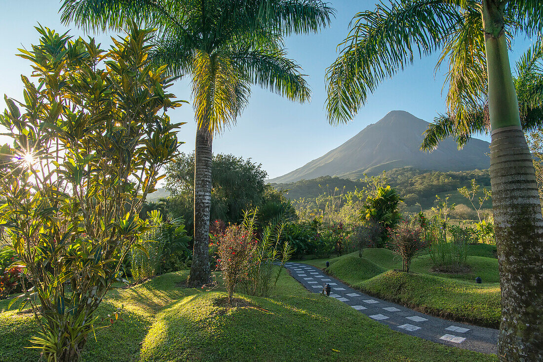 Looking through a tropical landscape with a stone pathway towards the sun rising over the Arenal Volcano; Alajuela Province, Costa Rica
