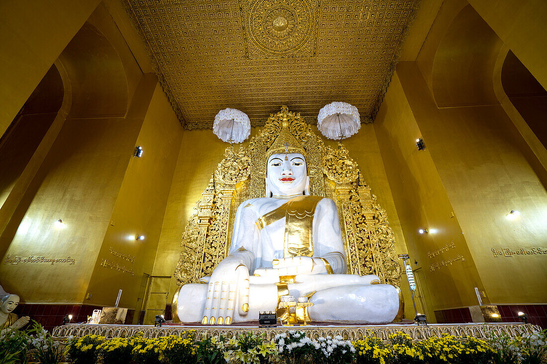 Interior of the Mahagandhayon Monastery with a white marble statue of a Sitting Buddha with gilded accessories and surrounded by golden walls; Amarapura, Mandalay City, Mandalay, Myanmar (Burma)