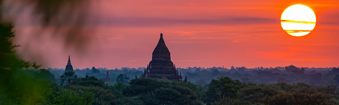 Silhouettes of pagodas with the sun rising above the Plain of Bagan at dawn; Bagan, Mandalay, Myanmar (Burma)