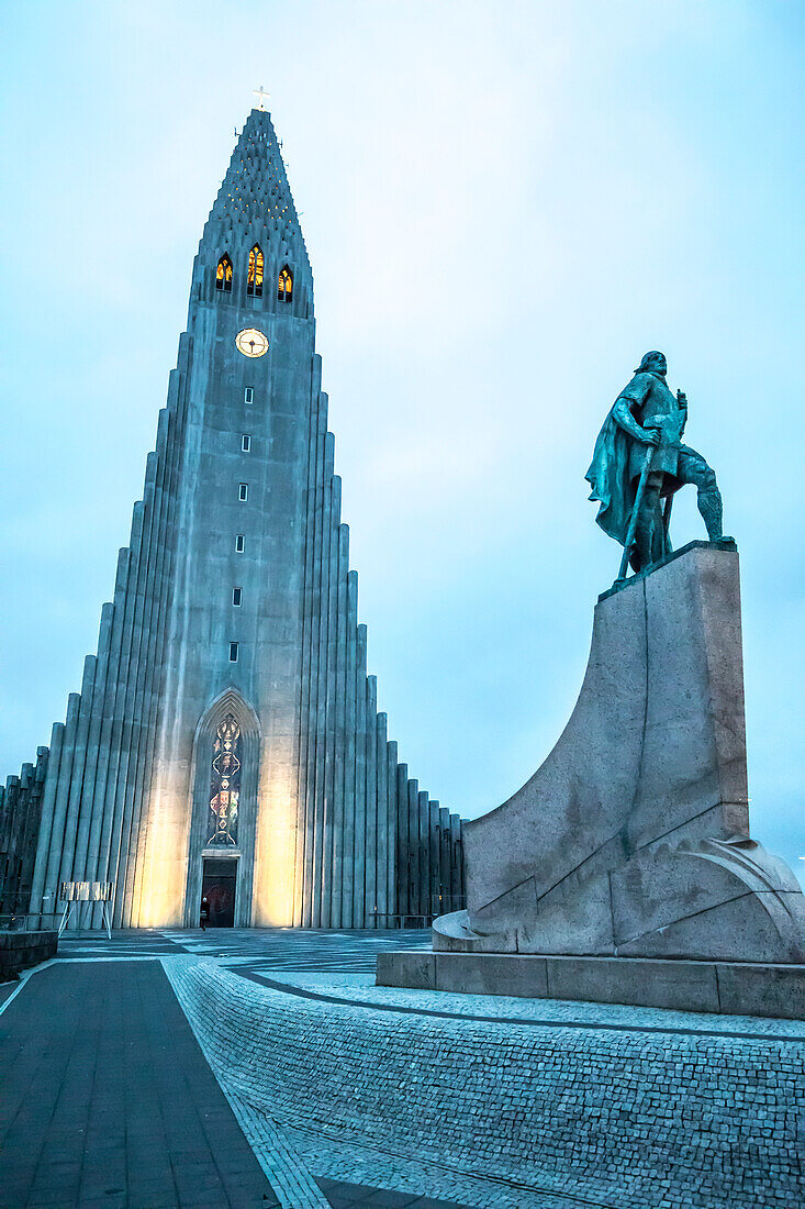Die beleuchtete Hallgrimskirkja, lutherische Kathedrale mit einer Statue des berühmten Entdeckers Leif Erikson im Vordergrund, der vor der Kirche als erster Europäer Amerika erreichte; Reykjavik, Hauptstadtregion, Island.
