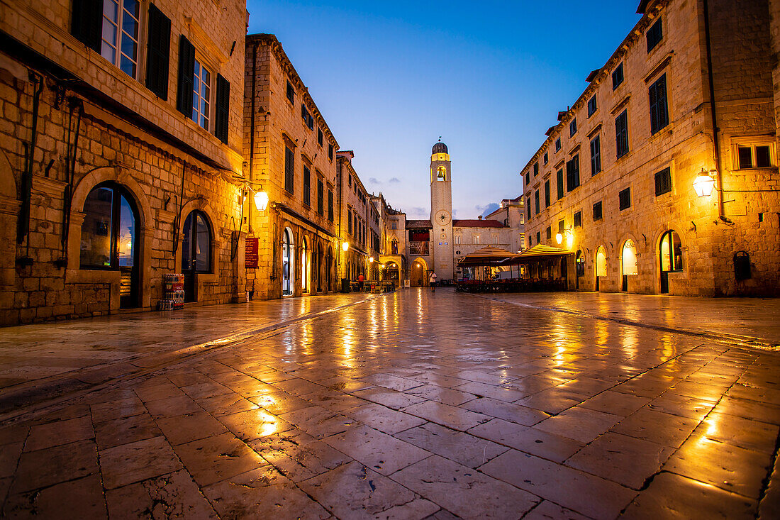 Light reflecting on the stone tiles of Luza Square in the Old Town, looking down to the Clock Tower against the dusk sky; Dubrovnik, Dalmatia, Croatia