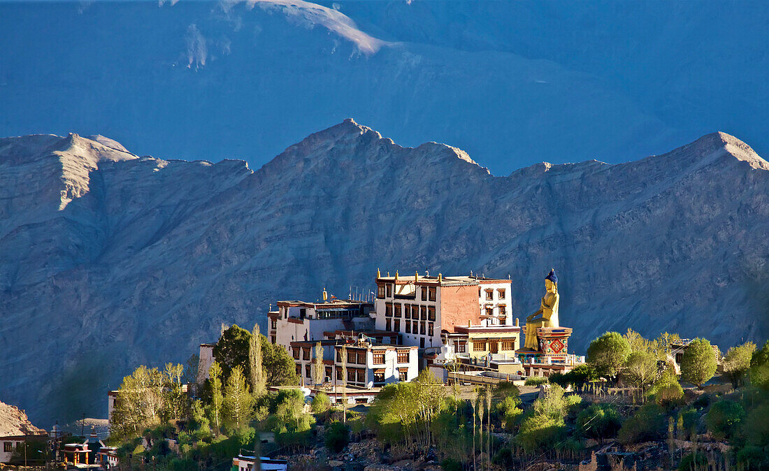 Überblick über die Dächer des Klosters Likir mit seiner riesigen vergoldeten Statue eines sitzenden Buddhas, der von oberhalb des Indus-Tals wacht, in den Himalaya-Bergen von Ladakh, Jammu und Kaschmir; Likir, Ladakh, Indien.