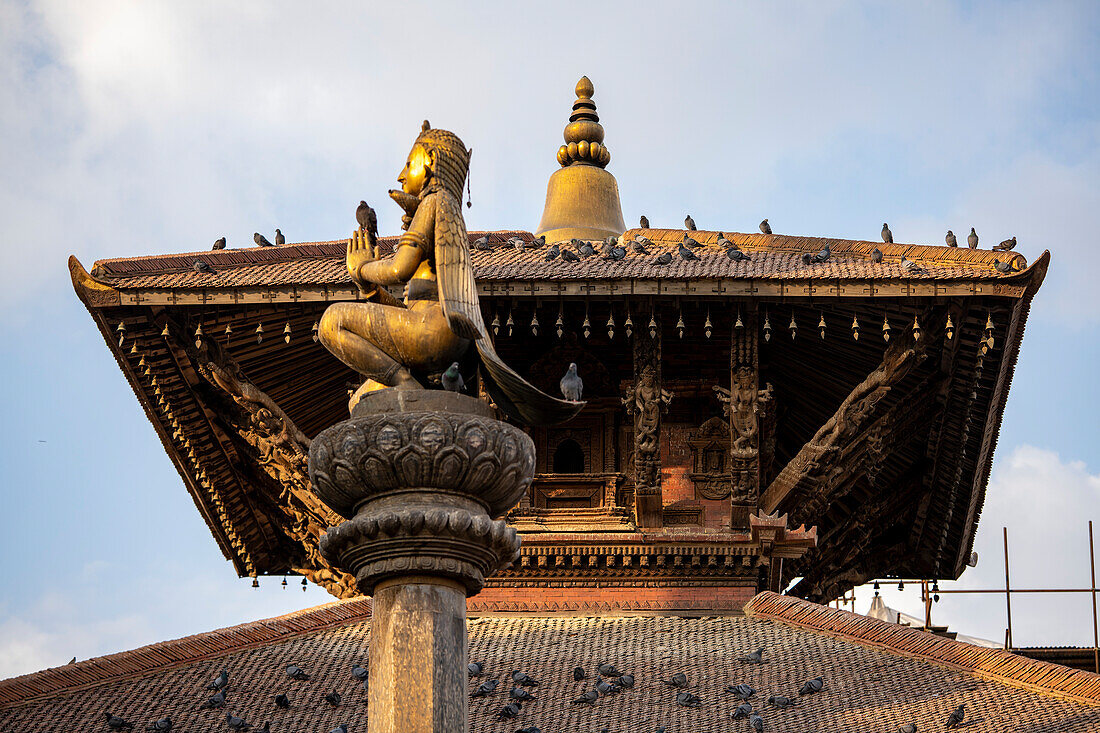 Column statue of Garuda at Durbar Square in the old city of Patan (or Lalitpur) in front of pagoda style rooftop built by the Newari Hindu Mallas between the 16th and 18th centuries in the Kathmandu Valley; Patan (Lalitpur), Kathmandu Valley, Nepal