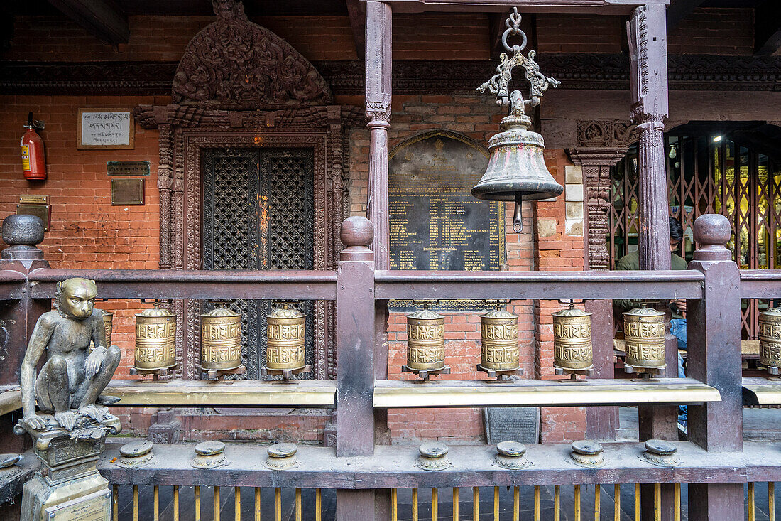 Affenfigur aus Messing neben einem Balkon mit Gebetsmühlen und Glocke im Goldenen Kwa Bahal-Tempel in der alten Stadt Patan oder Lalitpur, der im zwölften Jahrhundert von König Bhaskar Varman im Kathmandutal erbaut wurde; Patan (Lalitpur), Kathmandutal, Nepal.