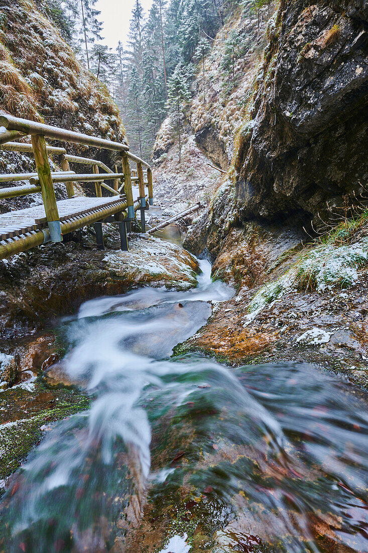 Nahaufnahme eines verschneiten Flusses mit einem Steg, der sich um die felsige Schlucht bei Janosikove Diery im Winter schlängelt; Kleine Fatra, Karpaten, Terchova, Slowakei.