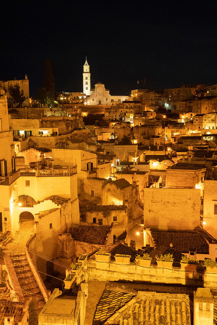 Nächtliches Stadtpanorama der antiken Höhlenwohnungen mit dem Glockenturm der Kathedrale von Matera über der Stadt; Matera, Basilikata, Italien