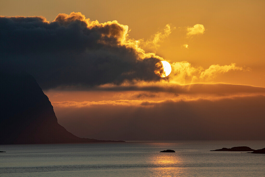 Mitternachtssonne leuchtet hinter den Wolken und spiegelt sich auf dem Nordatlantik; Lofoten, Polarkreis, Norwegen