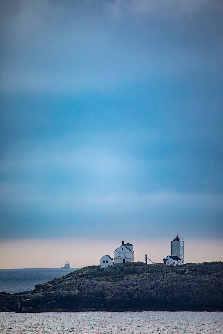 Terningen Lighthouse at twilight on a remote island in the Municipality of Hitra near the mouth of the Hemnfjorden with a ship on the horizon in the Western Fjords of Norway; Sor-Trondelag, Trondelag, Norway
