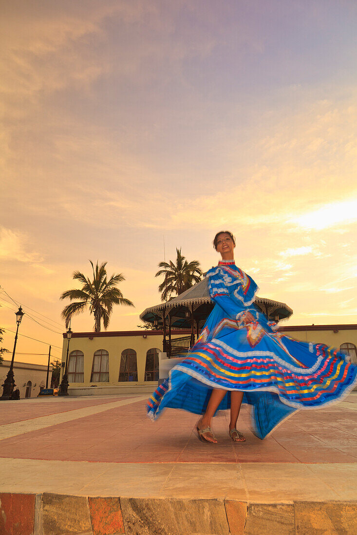 Eine Frau tanzt in einem traditionellen folkloristischen Kleid am frühen Morgen in der Innenstadt; Todos Santos Baja California Sur Mexiko