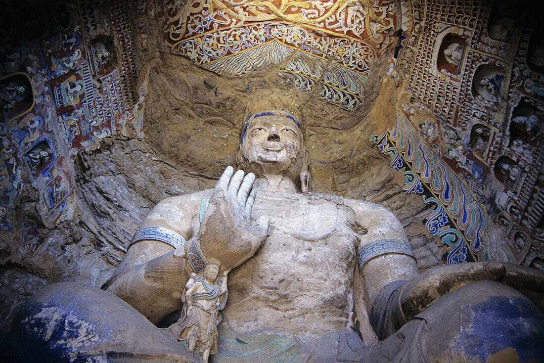 China, Datong, Detail of large Buddha statue seen from below surrounded by colorful paintings and carvings; Yungang Caves